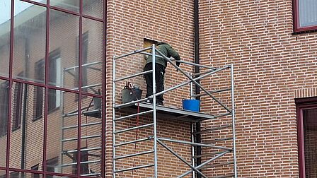 Een medewerker staat op de steiger om de vleermuiskast in de muur van het gemeentehuis te plaatsen.